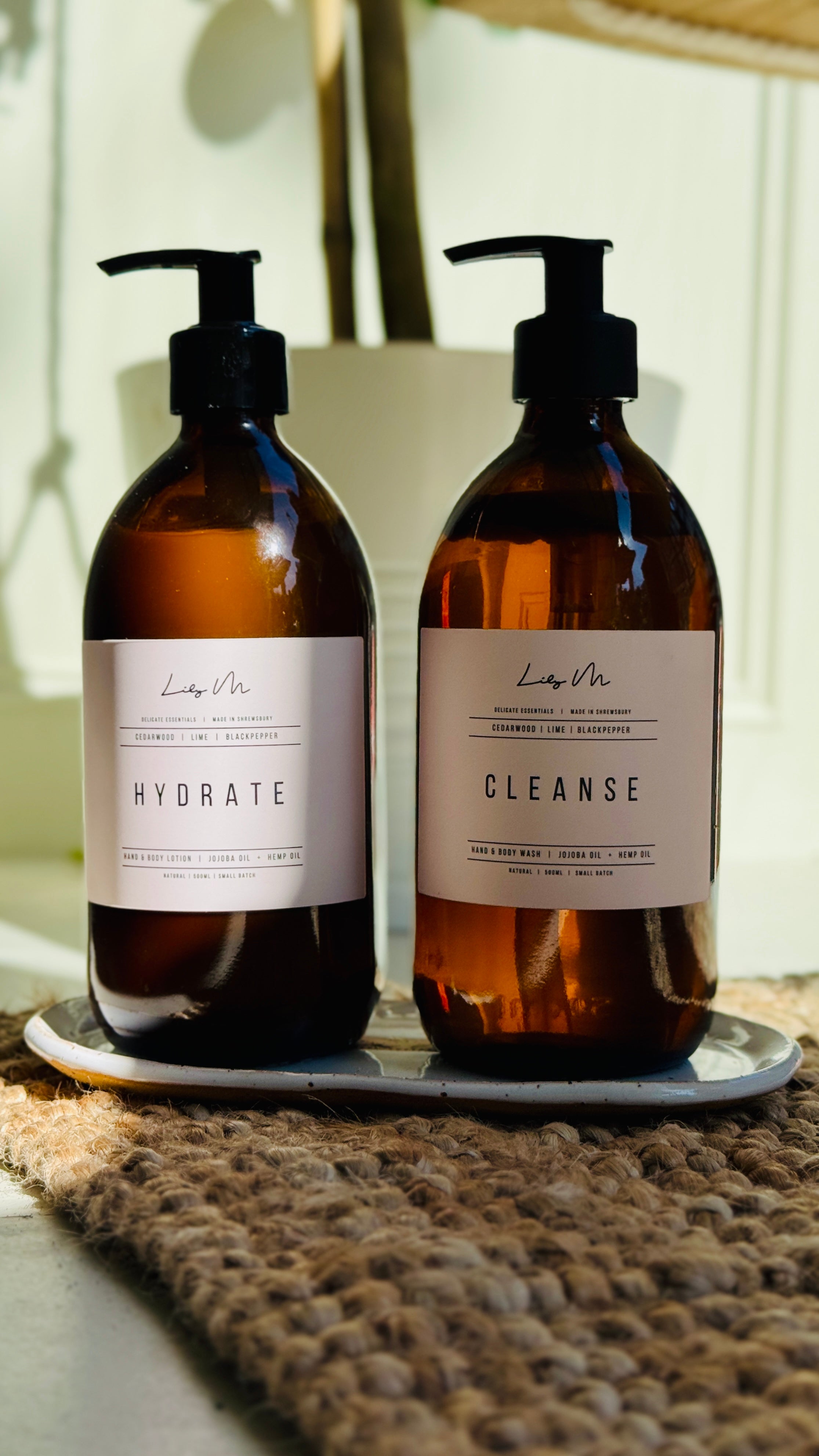 close up image on the two hand & body wash and lotion on the white glazed stone ware tray, with sunlight shinning on them