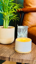 handmade white glaze candle jar on a small wooden table with a plant and card in the background
