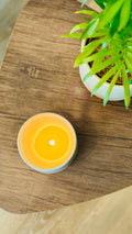 handmade white glaze candle jar on a small wooden table plant to the right hand side - the candle is lit