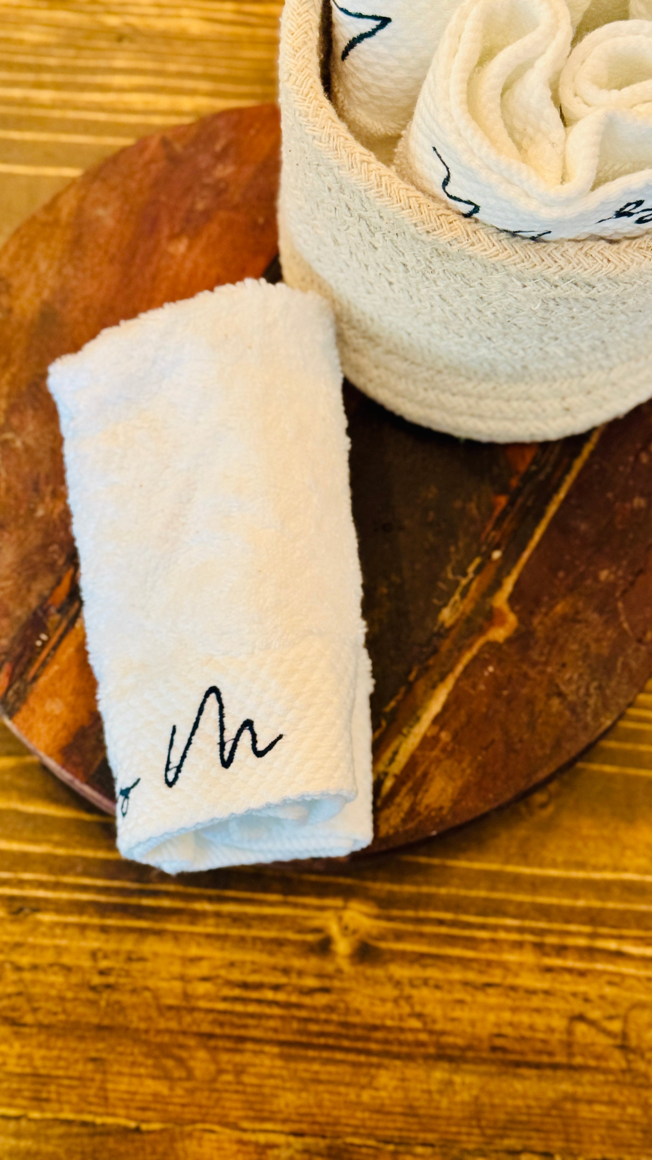 lily M branded face towel without a sleeve around it and a basket full of towels at the top of the image on a wooden tray