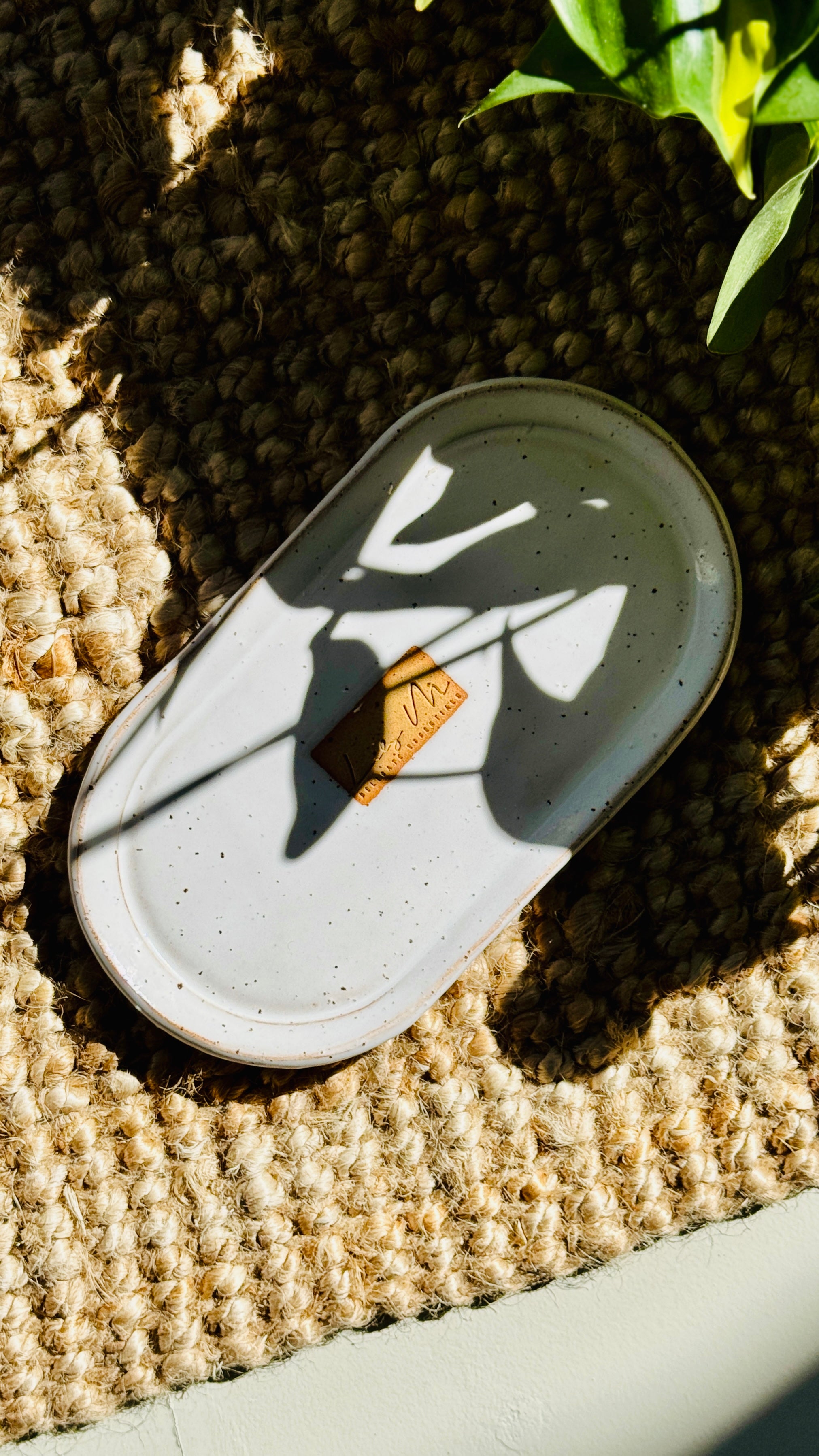 hand wash bottle tray on a hessian rug Lily M logo stamped in the the center of the tray unglazed, shows a brown rectangle around the logo, plant shadow over the tray