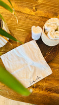 Lily M Branded face towel with an leaf in the foreground, and a basket of towels next to the opened up towel