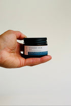 Hand holding a small jar of deodorant balm against a plain background