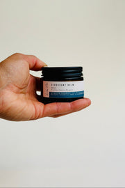 Hand holding a small jar of deodorant balm against a plain background