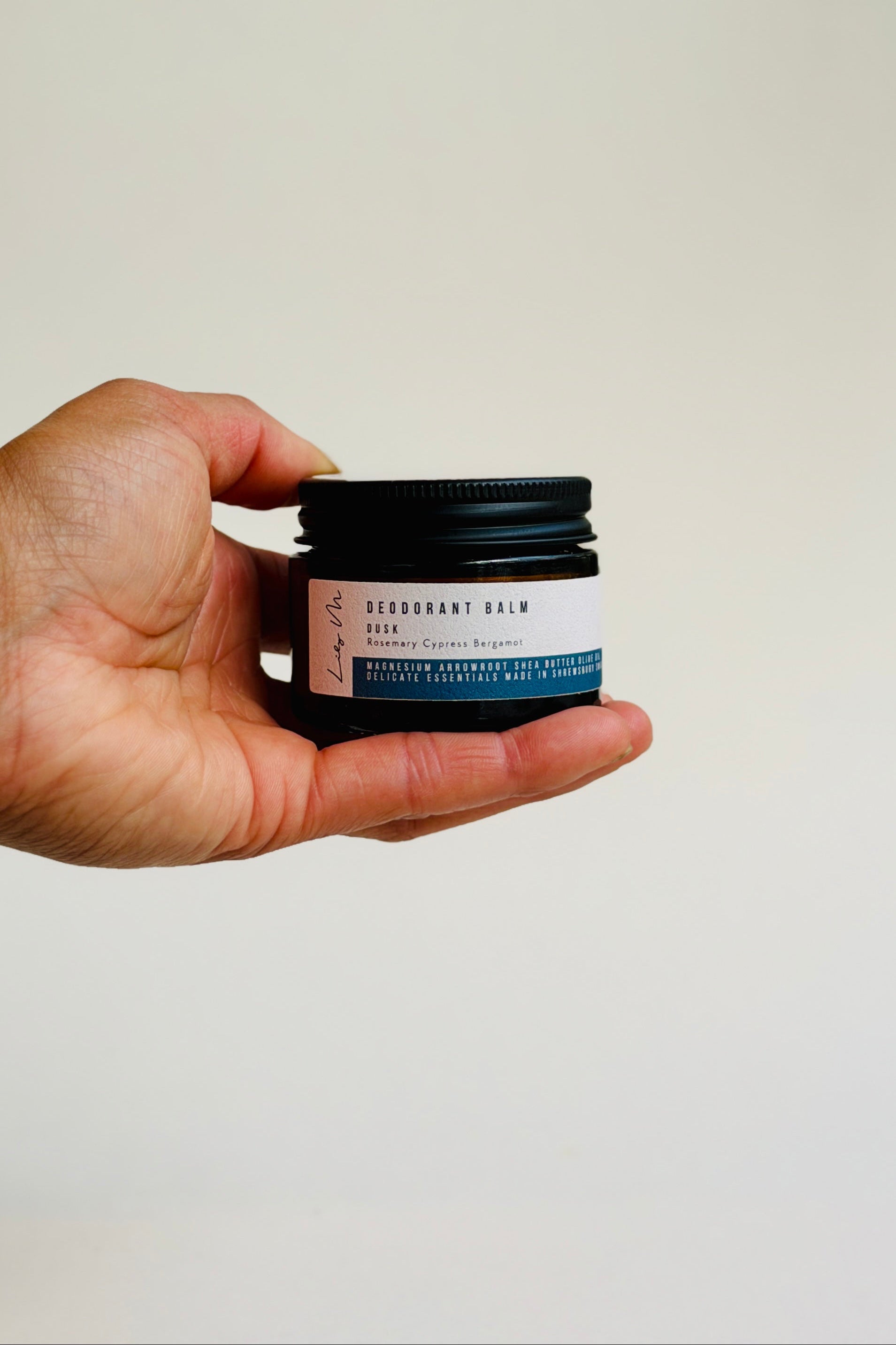 Hand holding a small jar of deodorant balm against a plain background