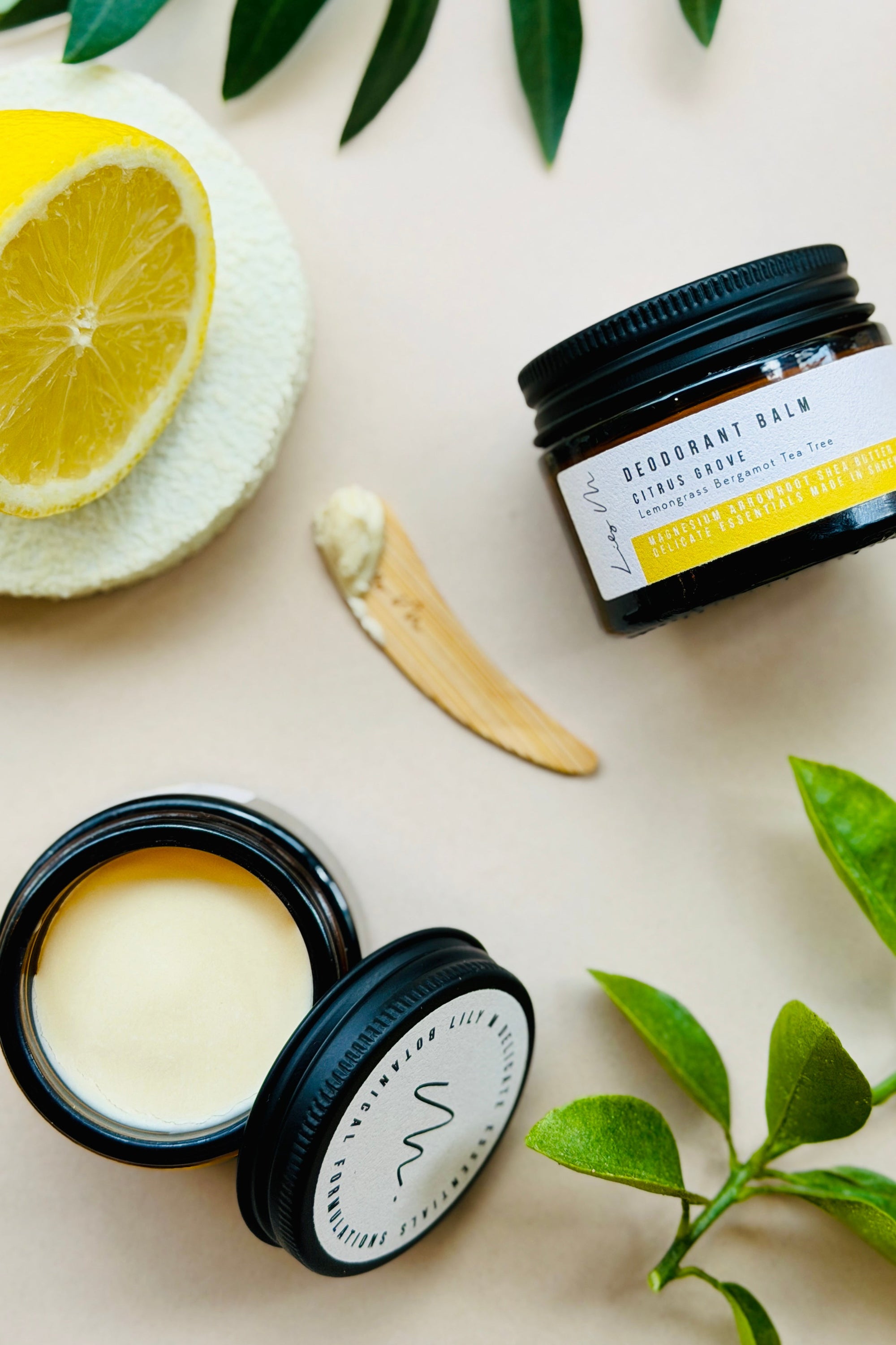Two open black containers of skincare product with a lemon and leaves on a light background