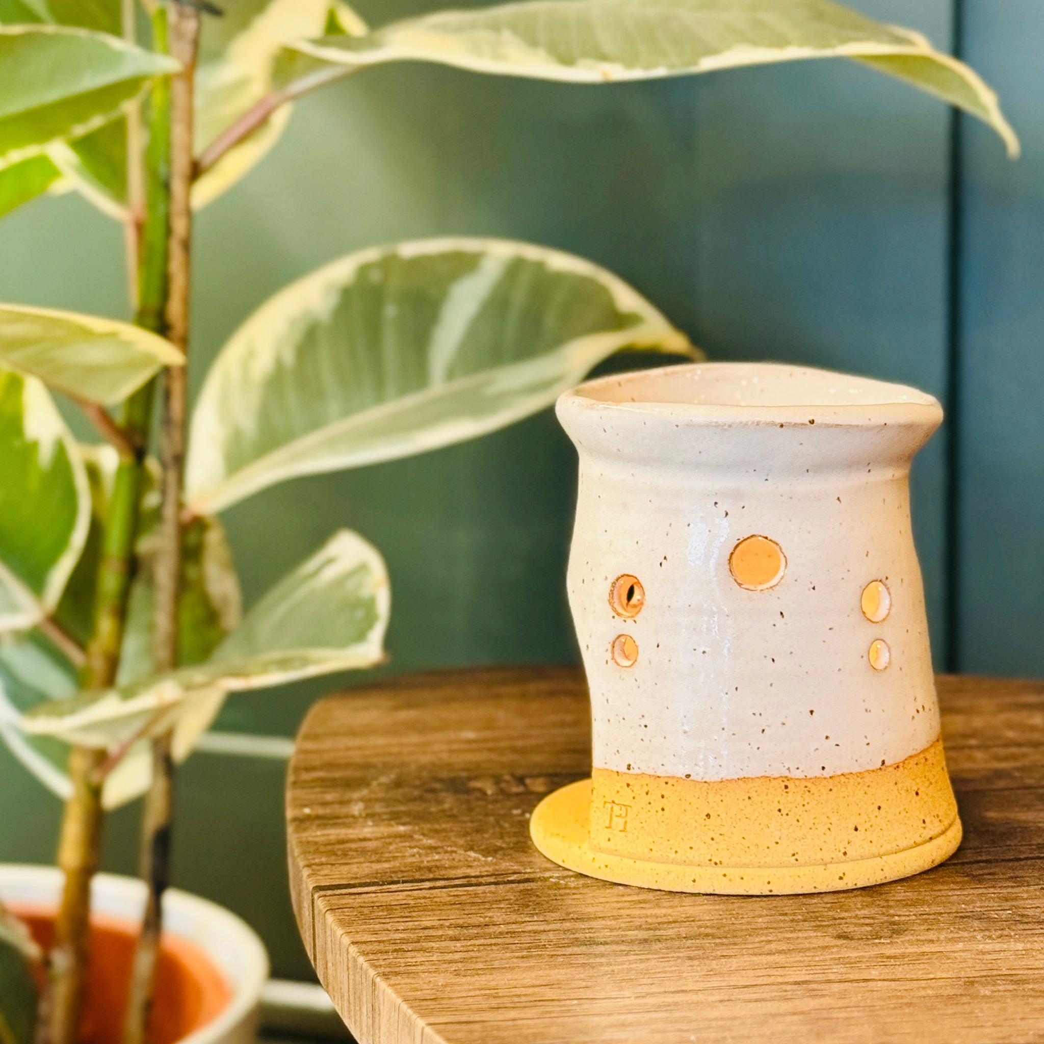 handmade wax melt burner in a white glaze, turn to the left on a wooden table with a plant in the left side of the image 
