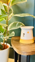 handmade wax melt burner in a white glaze, turn to theback on a wooden table with a plant in the left side of the image 