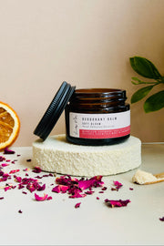Jar of deodorant balm on a white stand with an orange and dried flowers on a beige background