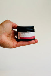Hand holding a small jar of deodorant cream against a plain background