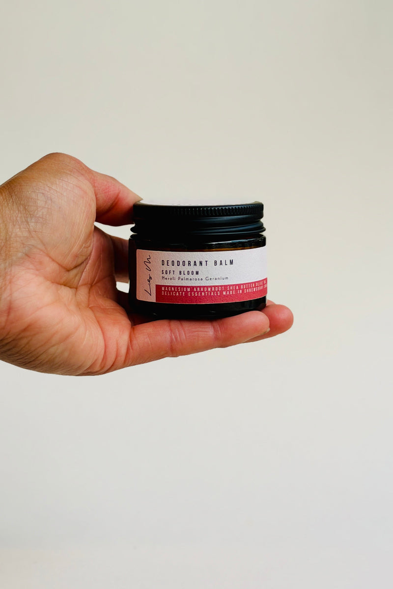 Hand holding a small jar of deodorant cream against a plain background