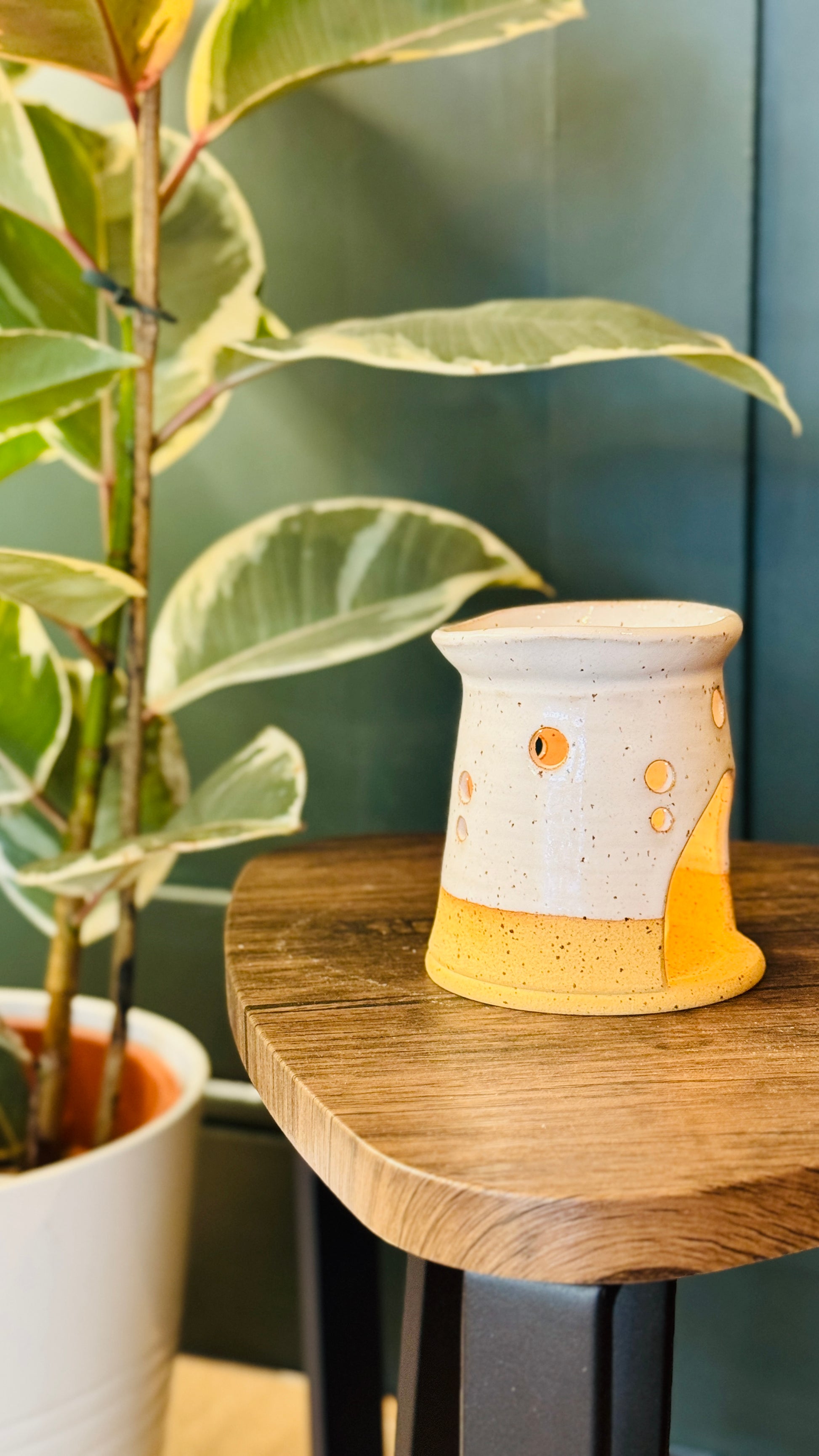 handmade wax melt burner in a white glaze, turn to the right on a wooden table with a plant in the left side of the image 